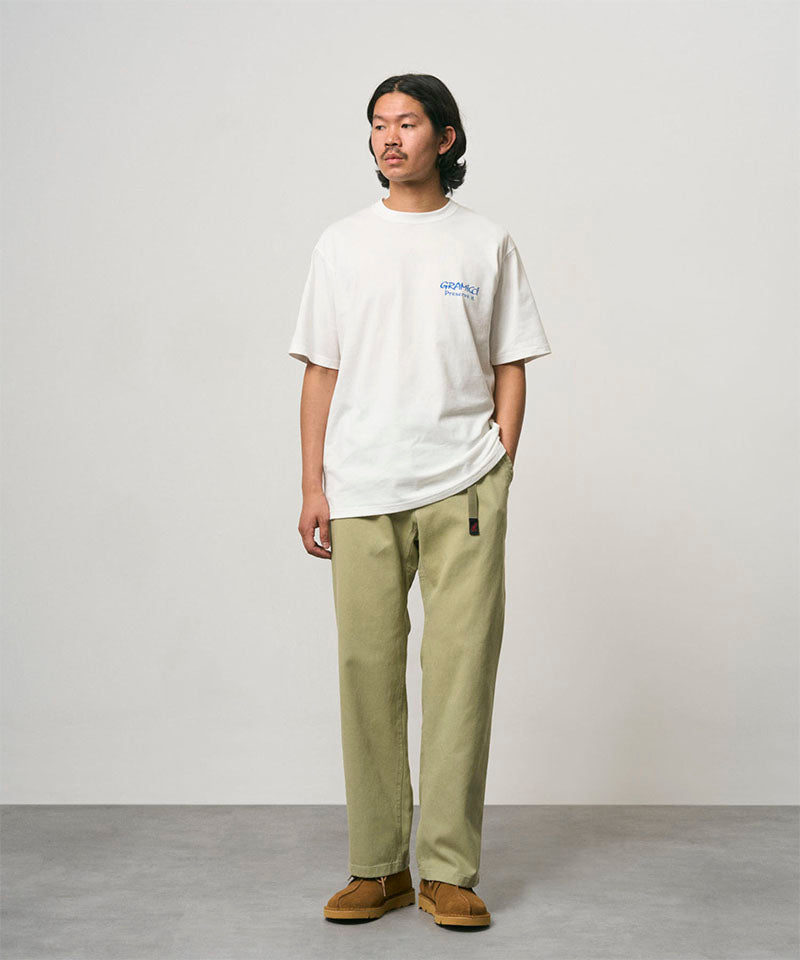 Model wearing a white Gramicci Earth Tee with a blue graphic and light olive pants on a light-tone background.