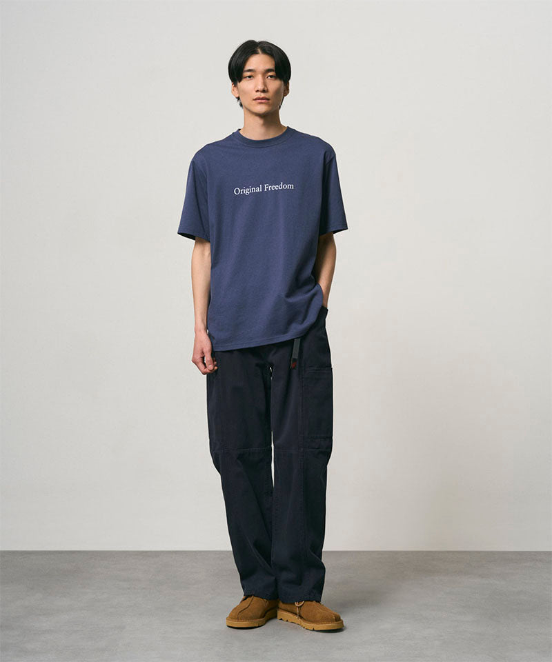 Model wearing a navy Gramicci Vase Tee and black pants on a light-tone background.