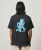 Back view of a model wearing a Gramicci vintage black Joker Tee with a teal graphic against a light-tone background.