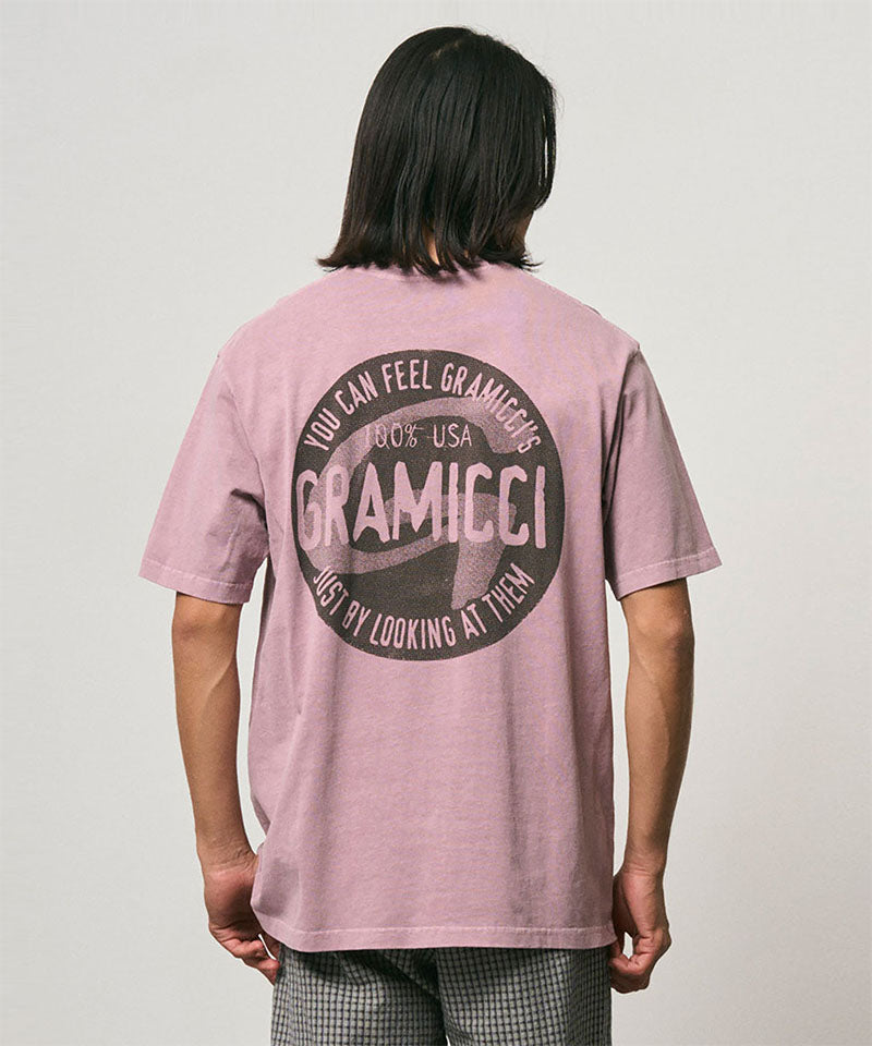 Back view of a model wearing a Gramicci lilac pigment colored Icon Tee Pigment Dyed with a graphic against a light-tone background.