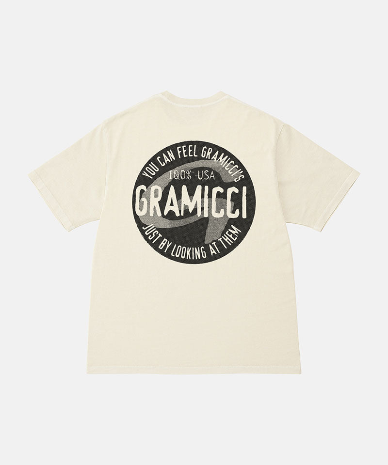 Back view of a Gramicci natural pigment colored Icon Tee Pigment Dyed with a graphic against a light-tone background.