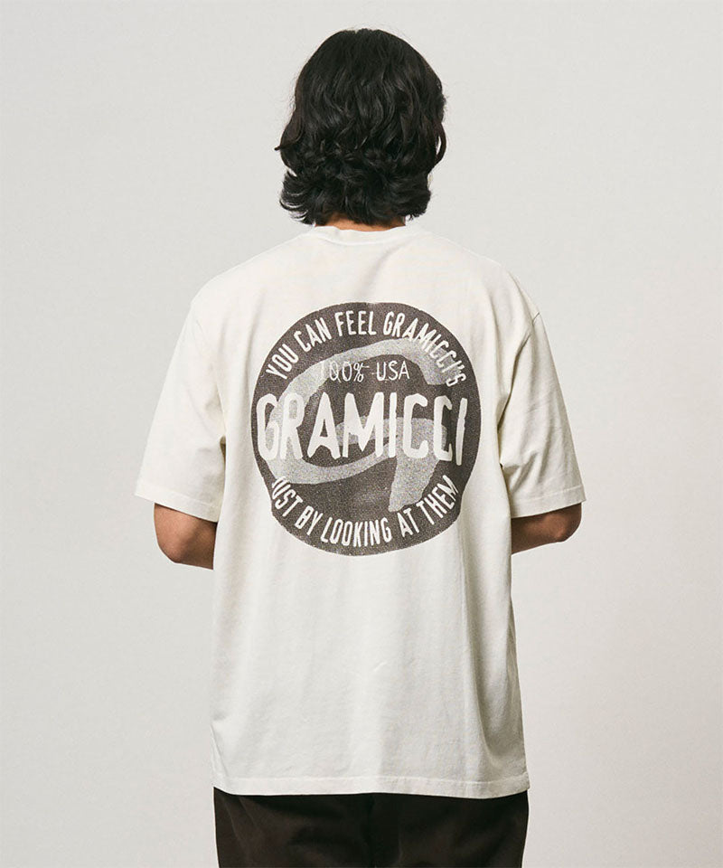 Back view of a model wearing a Gramicci natural pigment colored Icon Tee Pigment Dyed with a graphic against a light-tone background.