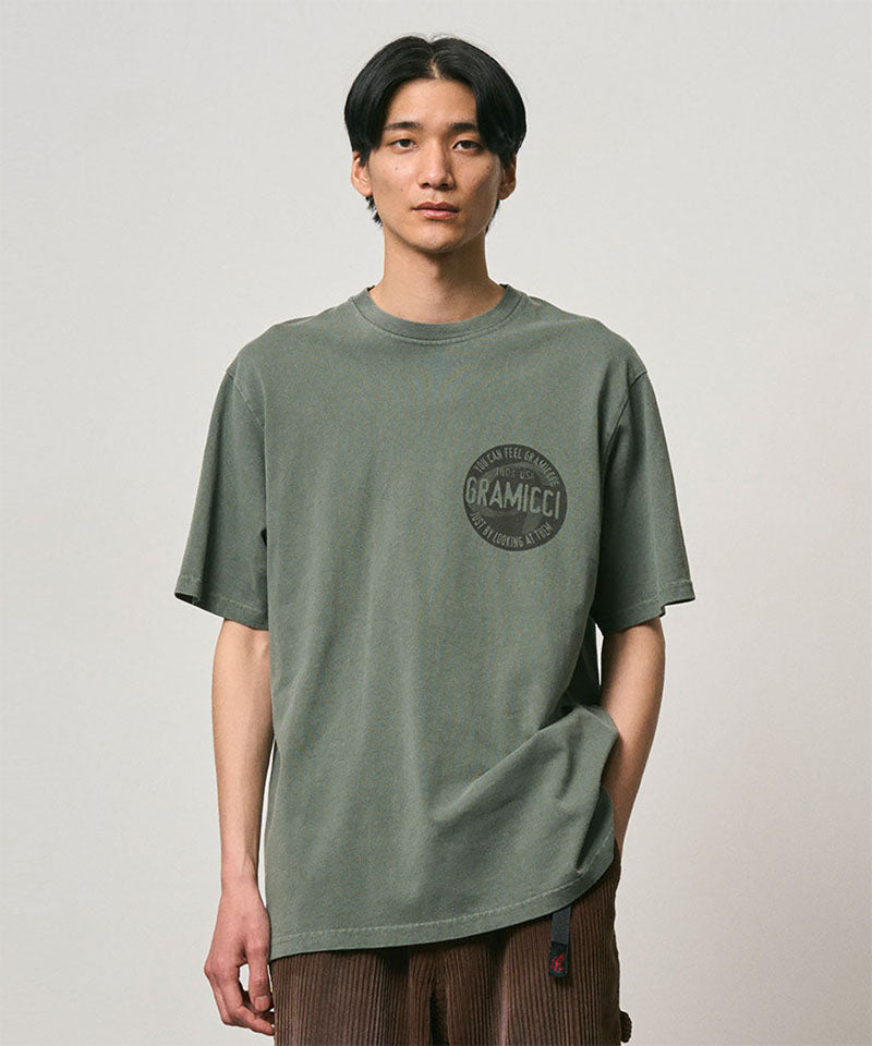 Model wearing a Gramicci sage pigment colored Icon Tee Pigment Dyed with a graphic against a light-tone background.