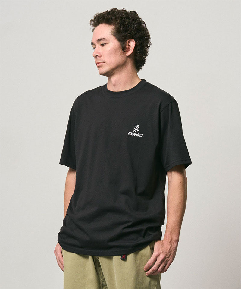 Model wearing a Gramicci black One Point Logo Tee with a graphic against a light-tone background.