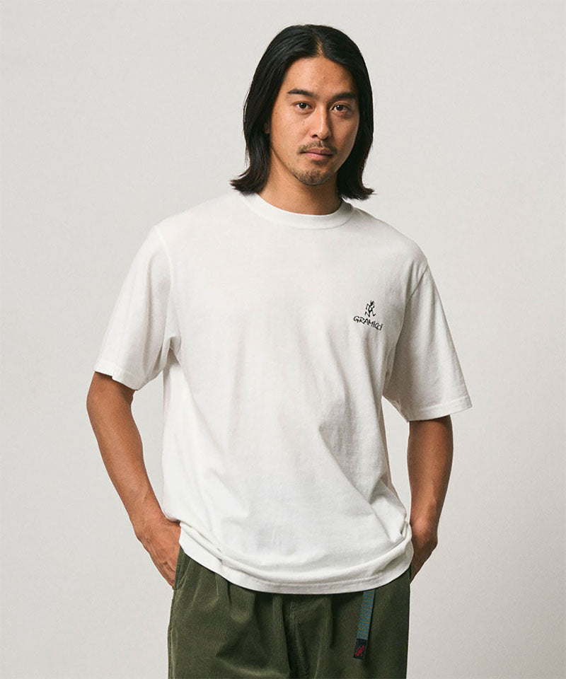 Model wearing a Gramicci white One Point Logo Tee with a graphic against a light-tone background.