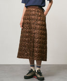 Model wearing a cola colored Gramicci G-Zero Primaloft Skirt and a blue shirt on a light-tone background.