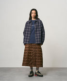 Model wearing a cola colored Gramicci G-Zero Primaloft Skirt and a blue plaid shirt on a light-tone background.