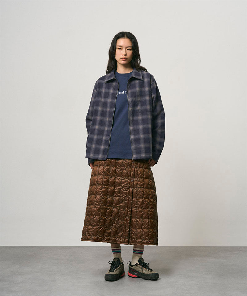 Model wearing a cola colored Gramicci G-Zero Primaloft Skirt and a blue plaid shirt on a light-tone background.