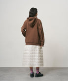 Back view of a model wearing a frost colored Gramicci G-Zero Primaloft Skirt and a brown hoodie on a light-tone background.