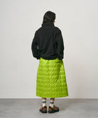 Model wearing a lime colored Gramicci G-Zero Primaloft Skirt and a black  jacket on a light-tone background.