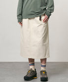 Model wearing a bone colored Gramicci Denim Carpenter Skirt and a olive shirt on a light-tone background.