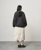 Back view of a model wearing a bone colored Gramicci Denim Carpenter Skirt and a dark brown jacket on a light-tone background.