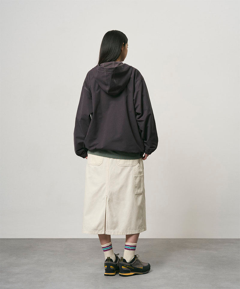 Back view of a model wearing a bone colored Gramicci Denim Carpenter Skirt and a dark brown jacket on a light-tone background.