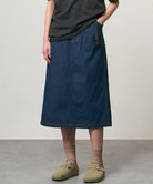 Model wearing a rinsed indigo Gramicci Denim Carpenter Skirt and a black shirt on a light-tone background.