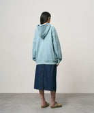 Back view of a model wearing a rinsed indego Gramicci Denim Carpenter Skirt and a light blue hoodie on a light-tone background.