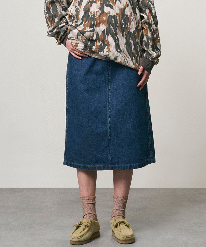 Model wearing a stone colored Gramicci Denim Carpenter Skirt and a camo sweatshirt on a light-tone background.