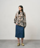 Model wearing a stone colored Gramicci Denim Carpenter Skirt and a camo sweatshirt on a light-tone background.