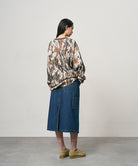 Back view of a model wearing a stone colored Gramicci Denim Carpenter Skirt and a camo sweatshirt on a light-tone background.