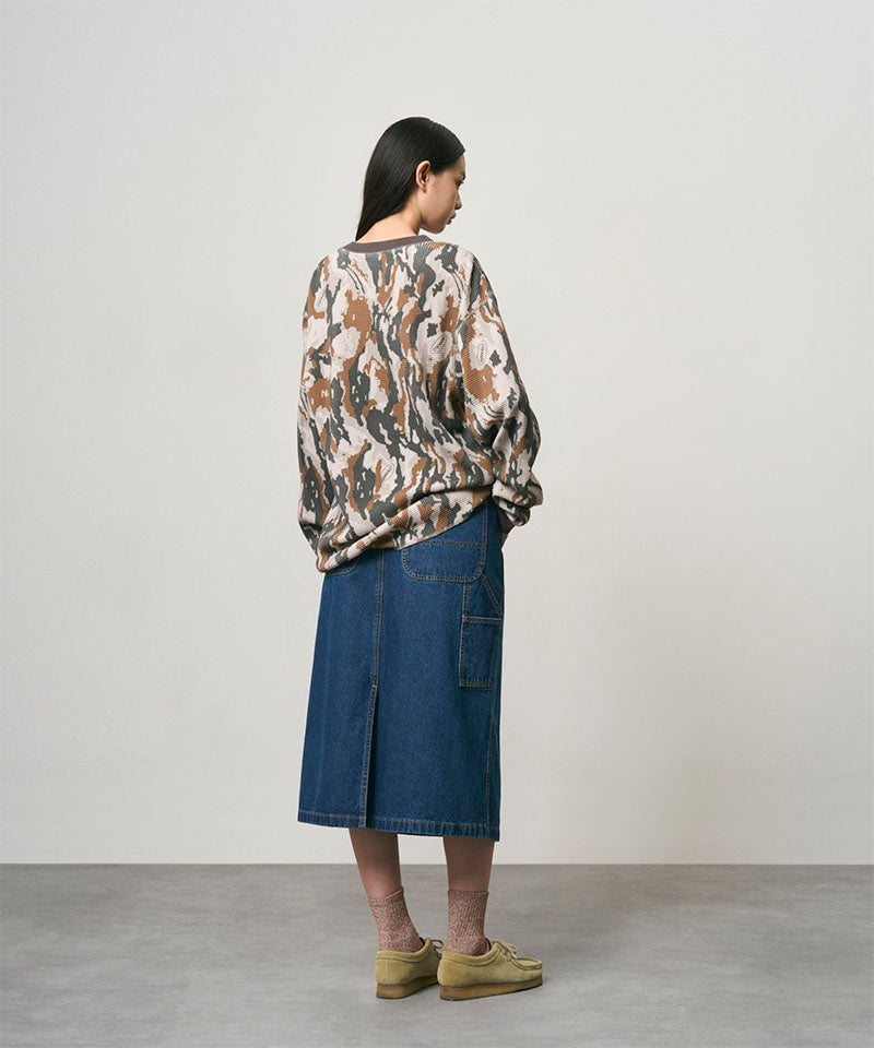 Back view of a model wearing a stone colored Gramicci Denim Carpenter Skirt and a camo sweatshirt on a light-tone background.