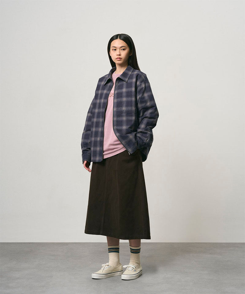 Model wearing a coffee colored Gramicci Venture Skirt and a blue plaid shirt on a light-tone background.