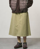 Model wearing a elm colored Gramicci Venture Skirt and a brown vest on a light-tone background.