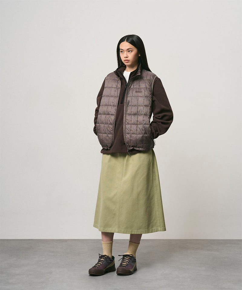 Model wearing a elm colored Gramicci Venture Skirt and a brown vest on a light-tone background.
