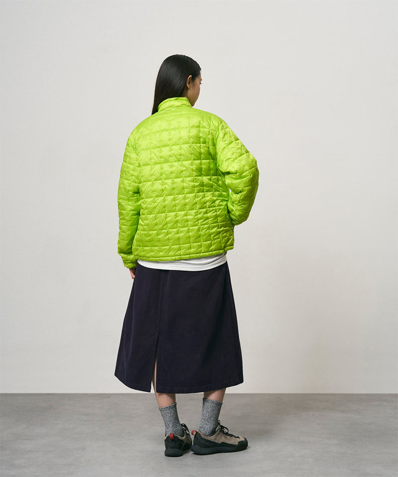 Back view of a model wearing a ink colored Gramicci Venture Skirt and a bright green jacket on a light-tone background.