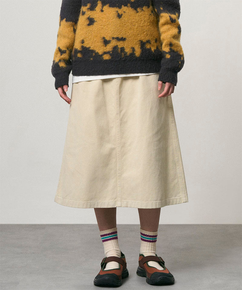 Model wearing a sand colored Gramicci Venture Skirt and a yellow and black tie-die sweater on a light-tone background.