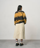 Back view of a model wearing a sand colored Gramicci Venture Skirt and a yellow and black tie-die sweater on a light-tone background.