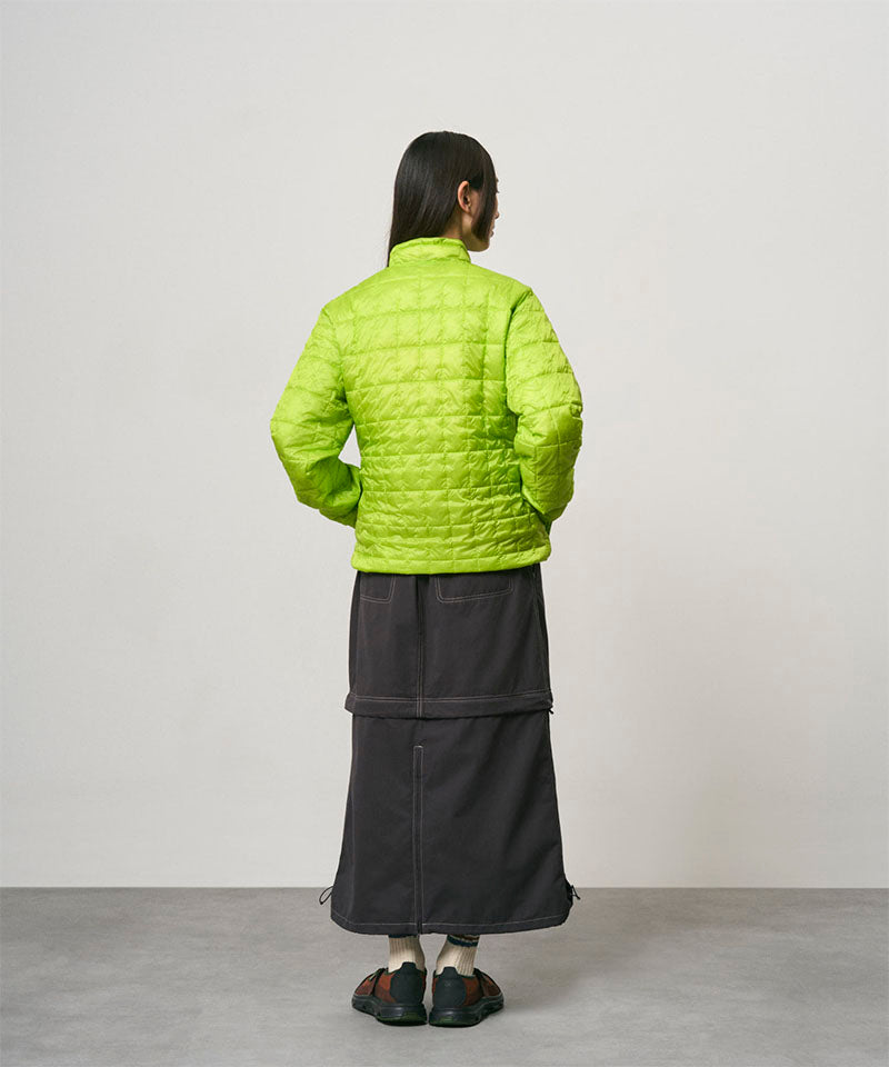 Back view of a model wearing a black women's Gramicci WR Convertible Skirt and a bright green jacket on a light-tone background.
