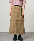 Model wearing a khaki colored women's Gramicci WR Convertible Skirt and a dusty pink shirt on a light-tone background.