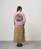 Back view of a model wearing a khaki colored women's Gramicci WR Convertible Skirt and a dusty pink shirt on a light-tone background.
