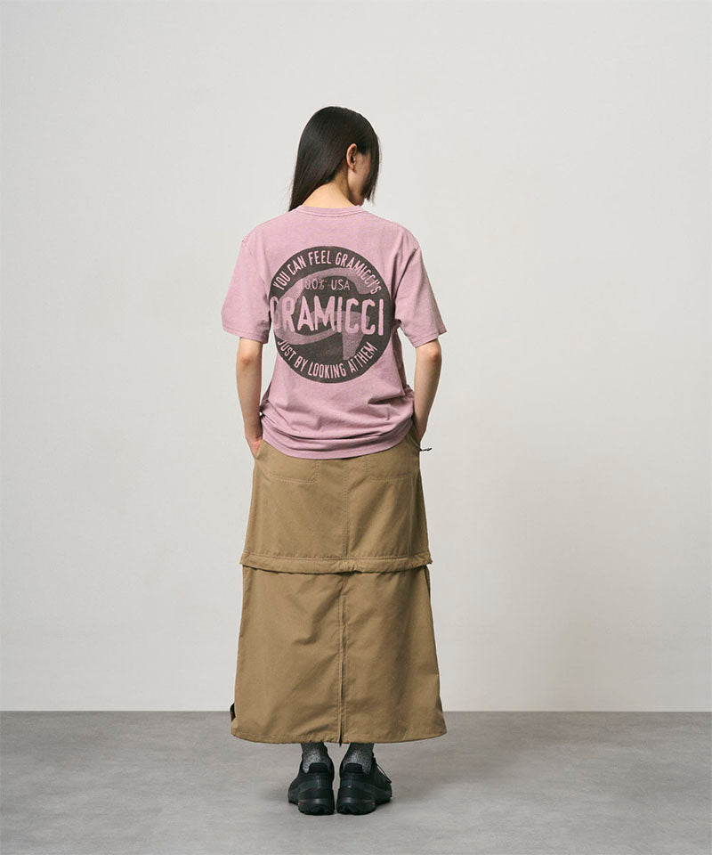 Back view of a model wearing a khaki colored women's Gramicci WR Convertible Skirt and a dusty pink shirt on a light-tone background.