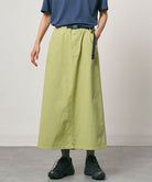 Model wearing a elm pigment colored Gramicci 5-Pocket Skirt and a blue shirt on a light-tone background.
