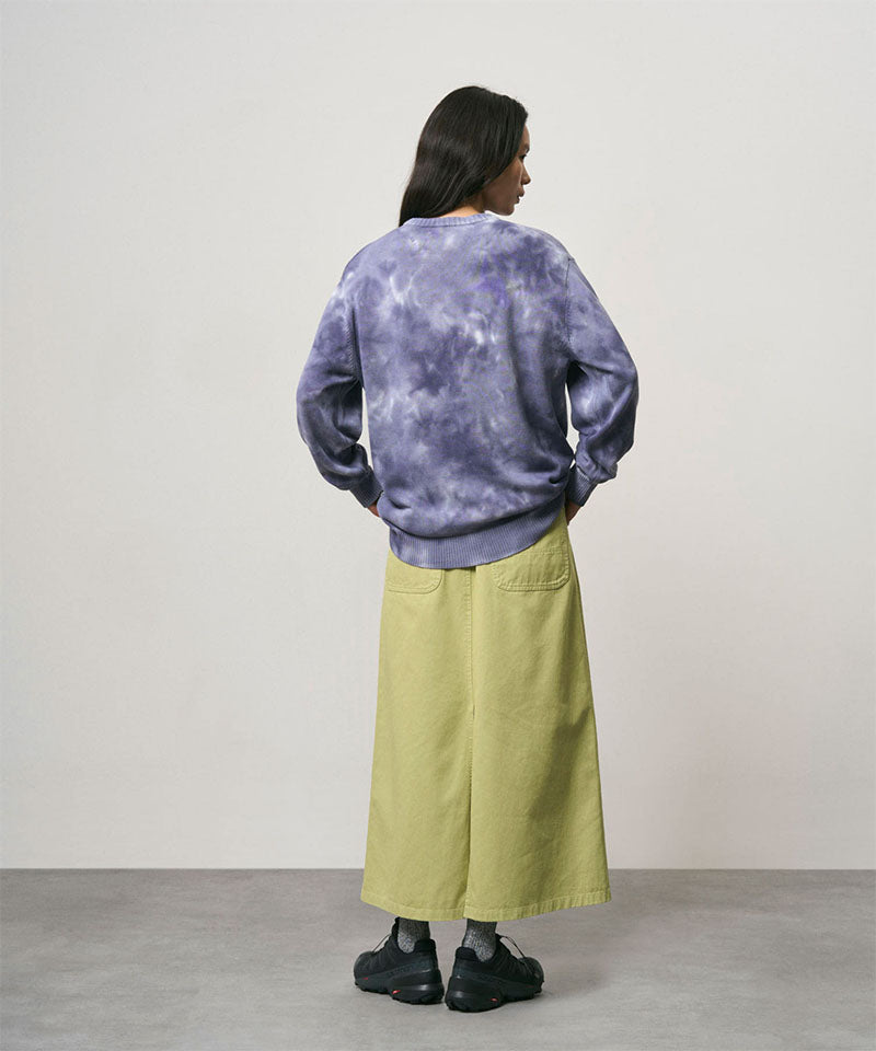 Back view of a model wearing a elm pigment colored Gramicci 5-Pocket Skirt and a purple tie-dye sweatshirt on a light-tone background.