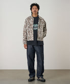 Model wearing a moss green Gramicci Taos Canvas Jacket and blue jeans on a light-tone background.