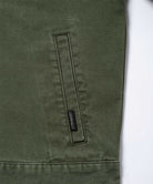 Close-up of a moss green Gramicci Taos Canvas Jacket on a light-tone background.