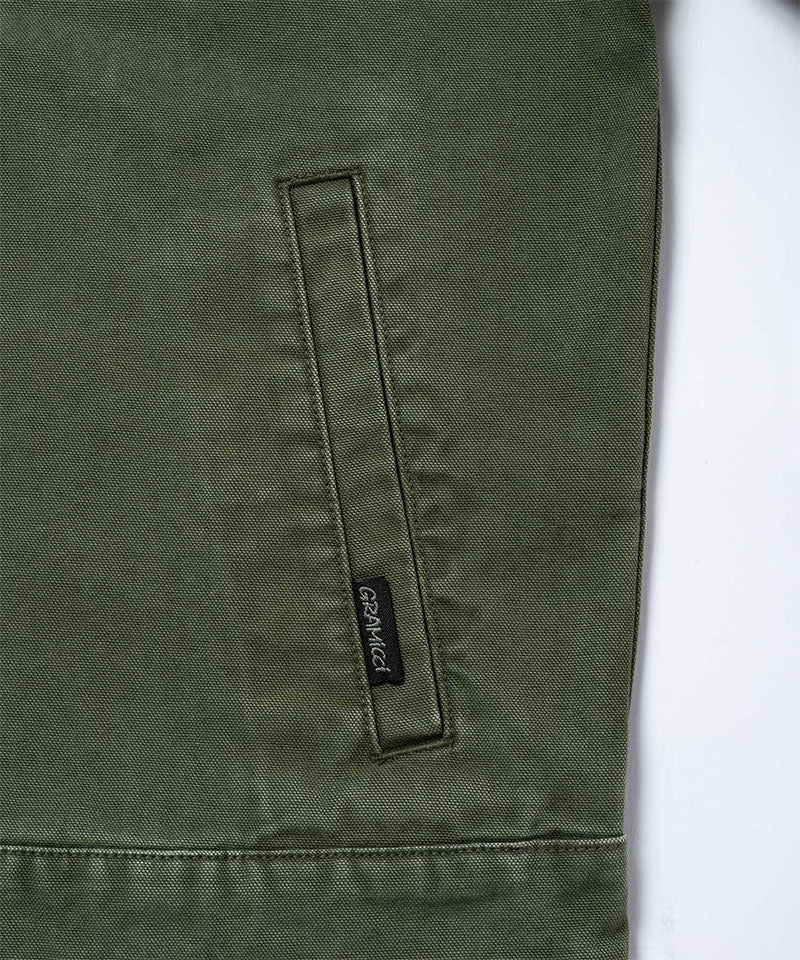 Close-up of a moss green Gramicci Taos Canvas Jacket on a light-tone background.