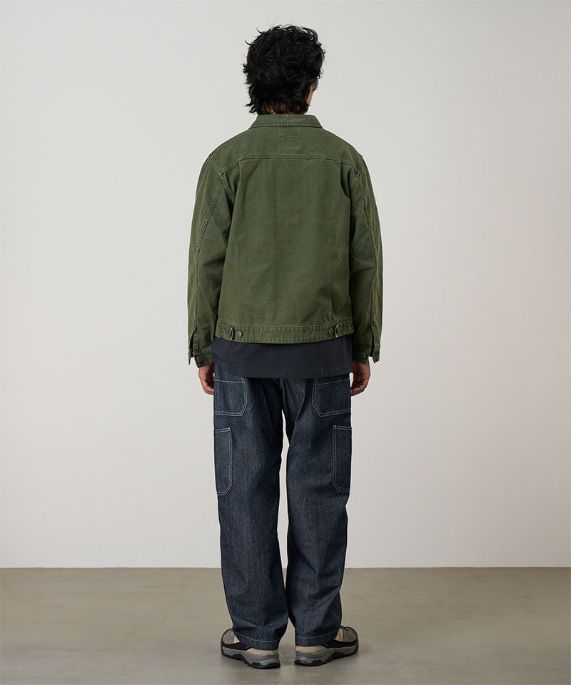 Back view of a model wearing a moss green Gramicci Taos Canvas Jacket and blue jeans on a light-tone background.