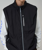 Person wearing a black vest over a white shirt with blue designs on a gray background