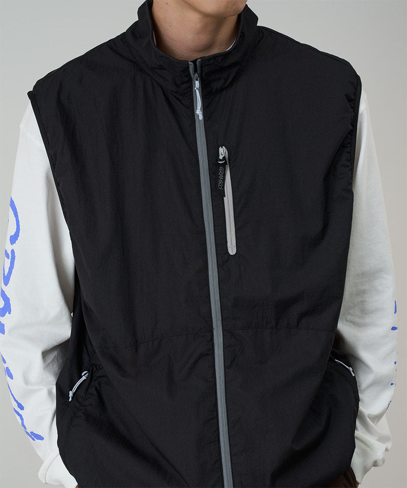 Person wearing a black vest over a white shirt with blue designs on a gray background