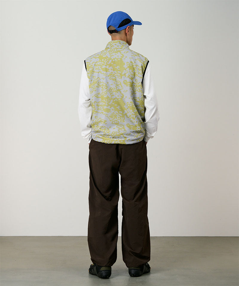 Person wearing a patterned vest, white shirt, brown pants, and blue cap on a plain background