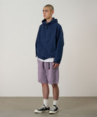 Model wearing a Gramicci Natural Dyed Jam Short in the color purple and a blue hoodie on a light-tone background.
