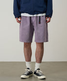 Model wearing a Gramicci Natural Dyed Jam Short in the color purple on a light-tone background.
