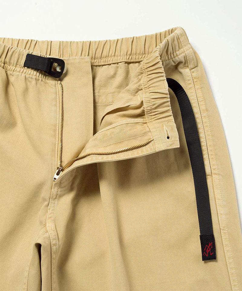 Close-up of Natural Dyed Gramicci Pant Straight Fit in the color chino with a black belt against a light-tone background.
