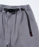 Close-up of natural dyed grey Gramicci Gadget Pants with a black belt on a light-tone background.
