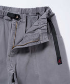 Close-up of natural dyed grey Gramicci Gadget Pants with a black belt on a light-tone background.
