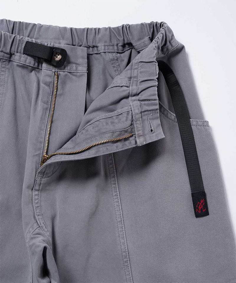 Close-up of natural dyed grey Gramicci Gadget Pants with a black belt on a light-tone background.
