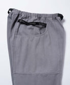 Close-up of natural dyed grey Gramicci Gadget Pants with a black belt and Gramicci branding on a light-tone background.
