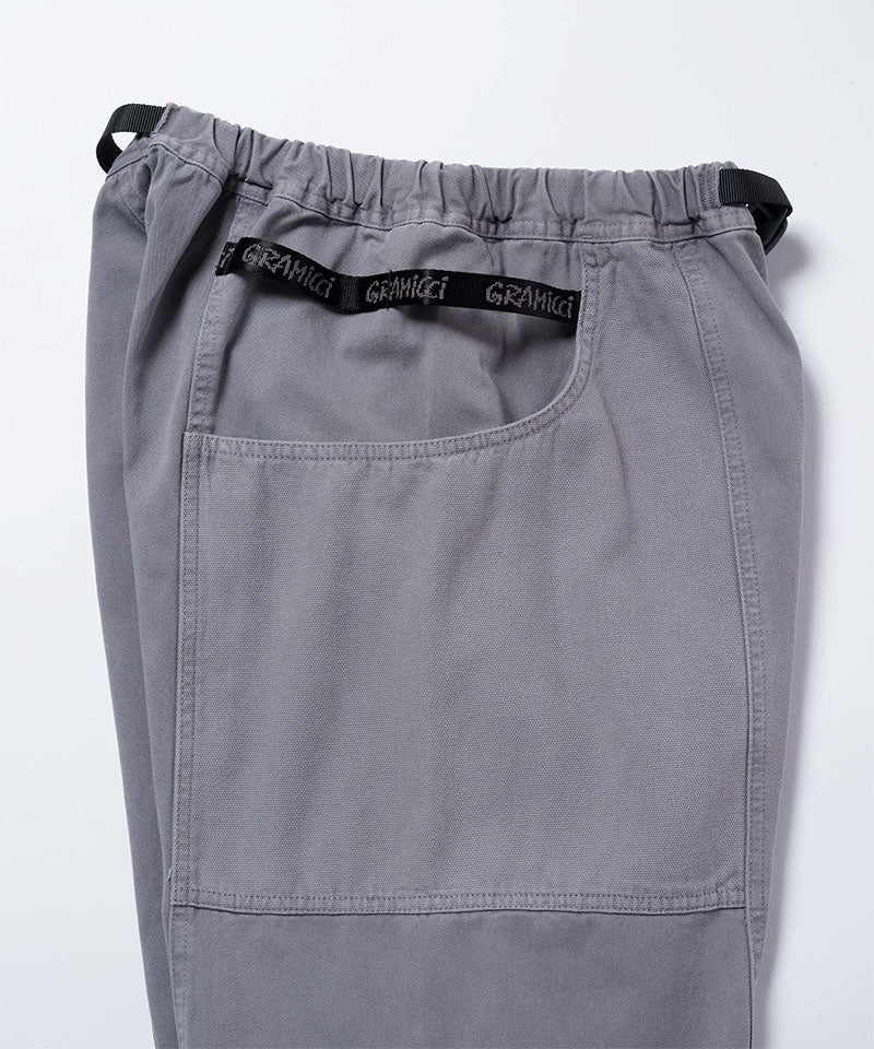 Close-up of natural dyed grey Gramicci Gadget Pants with a black belt and Gramicci branding on a light-tone background.
